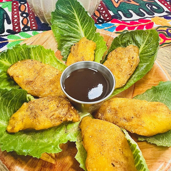 Golden fried Indian pakoras on lettuce leaves surrounding a dark dipping sauce on a wooden board.