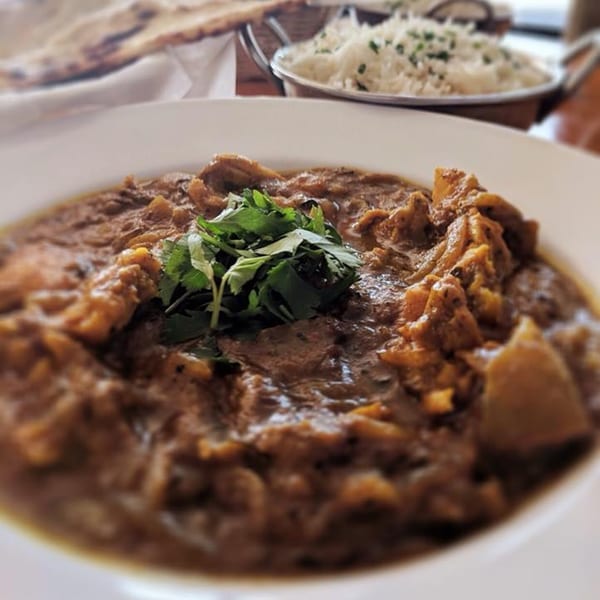 A bowl of rich Indian curry with cilantro, rice, and naan bread in the background.