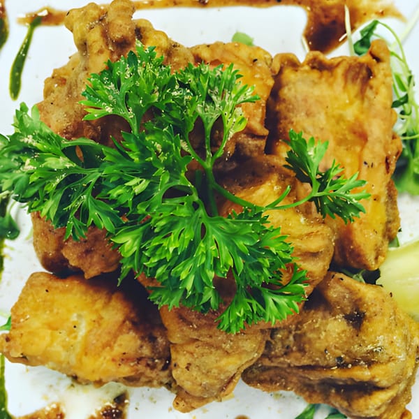 Crispy fried Indian pakora, garnished with fresh green parsley and a drizzle of sauce.